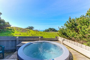 A hot tub on a wooden deck with a view of a grassy hill and trees. - Sea Ranch 3BR reverse-floor-plan home — hot tub & ocean views (Sea Ranch)