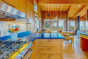 A kitchen with wooden cabinets, a gas stove, and a large island with a blue countertop. - Sea Ranch 3BR reverse-floor-plan home — hot tub & ocean views (Sea Ranch)