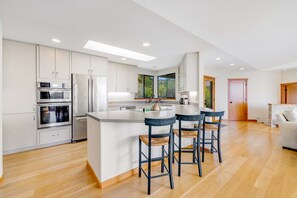 A modern kitchen with a central island, stainless steel appliances, and a large window. - Sea Ranch 3BR hot tub — Panoramic ocean-view home with priv (Sea Ranch)