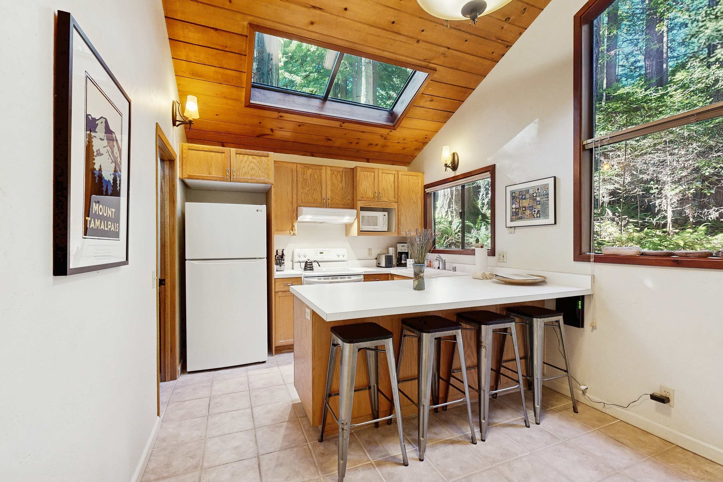 A kitchen with wooden cabinets, a white countertop, a skylight, and a large window with a forest view.