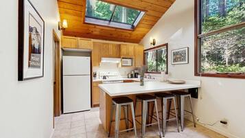 A kitchen with wooden cabinets, a white countertop, a skylight, and a large window with a forest view.