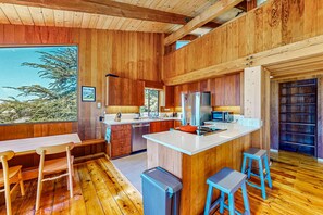 A wooden interior with a kitchen, dining area, and large windows. - Ocean-view home with hot tub & prime location at Shell Beach (Sea Ranch)
