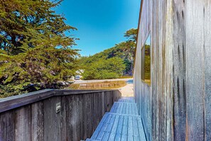 A wooden deck with a view of a forest and a road. - Ocean-view home with hot tub & prime location at Shell Beach (Sea Ranch)