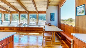 Un intérieur en bois comprenant un espace repas, des banquettes et de grandes fenêtres donnant sur l’extérieur.