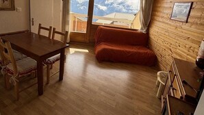 En inredning med träpanel, ett matbord, stolar, en soffa och en utsikt över bergen genom ett stort fönster.