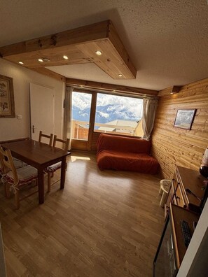 Ein Holzinterieur mit einem Esstisch, Stühlen, einer Couch und Blick auf Berge durch ein großes Fenster.