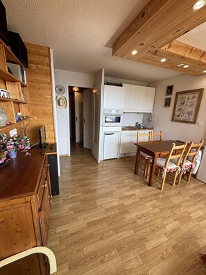 Eine Küche mit weißen Schränken, einem Holztisch mit Stühlen und einem Flur, der zu einer Tür führt.