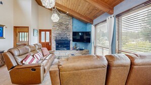 A living room with leather sofas, a stone fireplace, a flat-screen TV, and a wooden ceiling. - Sea Ranch 2BR home with private hot tub & game room — dog friendly (Sea Ranch)