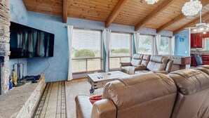 A spacious living area with a wooden ceiling, leather sofas, a flat-screen TV, and large windows. - Sea Ranch 2BR home with private hot tub & game room — dog friendly (Sea Ranch)