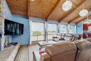 A spacious living area with a wooden ceiling, leather sofas, a flat-screen TV, and large windows.