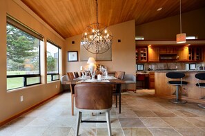 A spacious dining area with a large table, chairs, and a chandelier. - Sunsets over the ocean, waves, whales, serenity, luxury on the bluff (Sea Ranch)