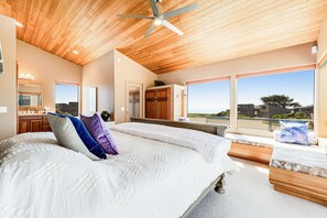 A bedroom with a large bed, wooden ceiling, and a view of the city. - Sunsets over the ocean, waves, whales, serenity, luxury on the bluff (Sea Ranch)