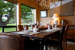 A dining table set with glassware, plates, and a candle, with a view of trees through large windows. - Coastal Luxury: Chef Kitchen, Ocean Views, Hot Tub (Sea Ranch)
