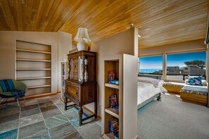 A bedroom with a bed, a wooden dresser, a chair, and a view of the ocean. - Coastal Luxury: Chef Kitchen, Ocean Views, Hot Tub (Sea Ranch)