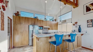 Eine moderne Küche mit Holzausstattung, einer zentralen Kochinsel mit Barhocker und großen Fenstern.