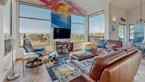 Ein großzügiges Wohnzimmer mit einem großen Fernseher, Ledersofas, einem Bücherregal und Blick auf die Landschaft.