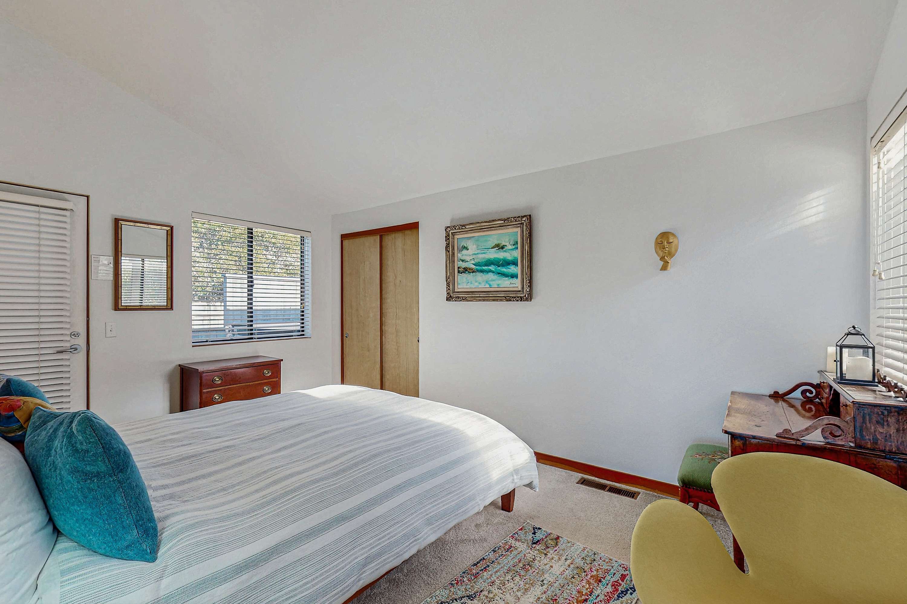 Un dormitorio con cama, cómoda, silla, ventana y un cuadro en la pared.