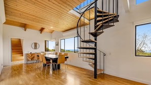 Een modern interieur met een wenteltrap, houten vloeren, een eethoek en grote ramen met uitzicht.