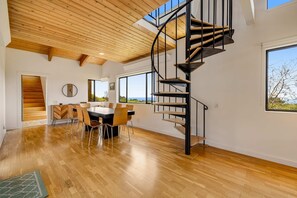 A modern interior with a spiral staircase, wooden flooring, a dining area, and large windows offering a view. - Sea Ranch 2BR modern home with hot tub & ocean views near Shell Beach (Sea Ranch)
