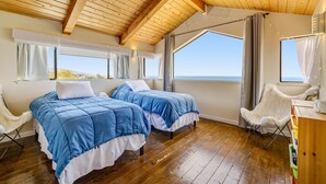 Een kamer met twee bedden, houten vloeren, grote ramen en uitzicht op zee.