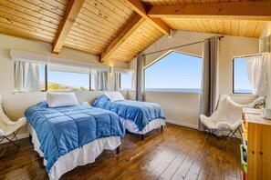 A room with two beds, wooden flooring, large windows, and a view of the sea. - Sea Ranch 2BR modern home with hot tub & ocean views near Shell Beach (Sea Ranch)
