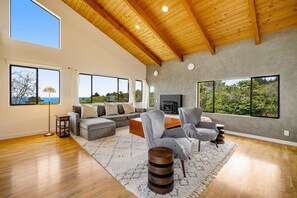 A spacious living room with a high ceiling, large windows, a fireplace, and a cozy seating area. - Sea Ranch 2BR modern home with hot tub & ocean views near Shell Beach (Sea Ranch)