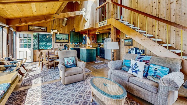 Un interior espacioso de madera con una escalera, un comedor y una sala de estar amoblada con sofás y sillones.