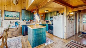 Una cocina rústica con paredes de madera, una isla central y una cabeza de animal colgada.