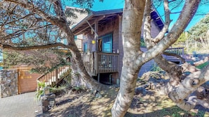 Une maison en bois dotée d’un balcon, entourée d’arbres et d’un mur de pierres.
