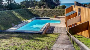 A pool with a wooden deck, a wooden building with a balcony, and a view of the ocean. - Sea Ranch 2BR ocean-view home with private hot tub & courtyard (Sea Ranch)