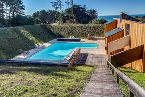 A pool with a wooden deck, a wooden building with a balcony, and a view of the ocean. - Sea Ranch 2BR ocean-view home with private hot tub & courtyard (Sea Ranch)