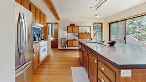 A modern kitchen with wooden cabinets, stainless steel appliances, and a large island with a sink. - Sea Ranch 2BR ocean-view home with private hot tub & courtyard (Sea Ranch)