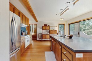 A modern kitchen with wooden cabinets, stainless steel appliances, and a large island with a sink. - Sea Ranch 2BR ocean-view home with private hot tub & courtyard (Sea Ranch)
