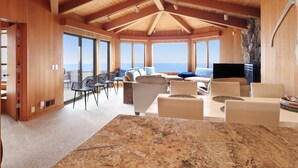 Una habitación amplia con techo alto, ventanas grandes, televisor de pantalla plana y comedor con mesa de granito.