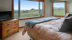 Un dormitorio con una cama, un aparador de madera, un televisor y dos ventanas que dan a un paisaje con césped.