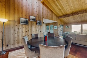 Ein Zimmer mit Holzwänden, einem runden Tisch, Stühlen, einer Couch und gerahmten Bildern an den Wänden.