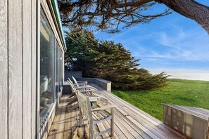 Eine Holzterrasse mit Sitzgelegenheiten, Blick auf ein saftiges Grasfeld und einen großen Baum.