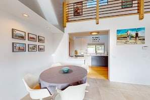 A dining area with a round table, white chairs, and a kitchen in the background.