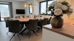 Un espace repas moderne avec une table en bois, des chaises noires et un grand vase rempli de fleurs.