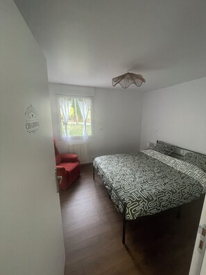 Ein kleines Schlafzimmer mit einem Bett, einem Fenster mit Vorhängen, einem roten Sessel und einem an der Wand befestigten Schild.