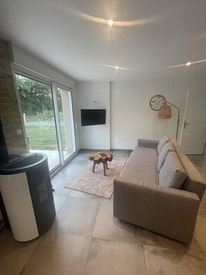 Un salon moderne avec un canapé, un téléviseur fixé au mur, une cheminée et une grande fenêtre.