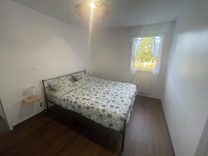 A small, single-bed room with a wooden floor, a window with a view of trees, and a ceiling light fixture. - Gîte de la Nolière - Normandy (La Lande-Saint-Siméon)