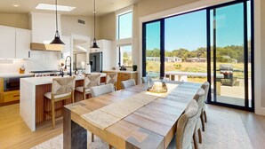 A modern kitchen with a central island, large windows, and a dining area with a view. - Luxe newly built Sea Ranch home with private hot tub & ocean views (Sea Ranch)