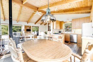 A spacious living area with a large wooden table, a ceiling fan, and a kitchen area with modern appliances. - Meadow home with private hot tub on the golf course (Sea Ranch)