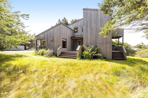 A modern wooden house with a large window, a front door, and a staircase leading to the entrance. - Meadow home with private hot tub on the golf course (Sea Ranch)