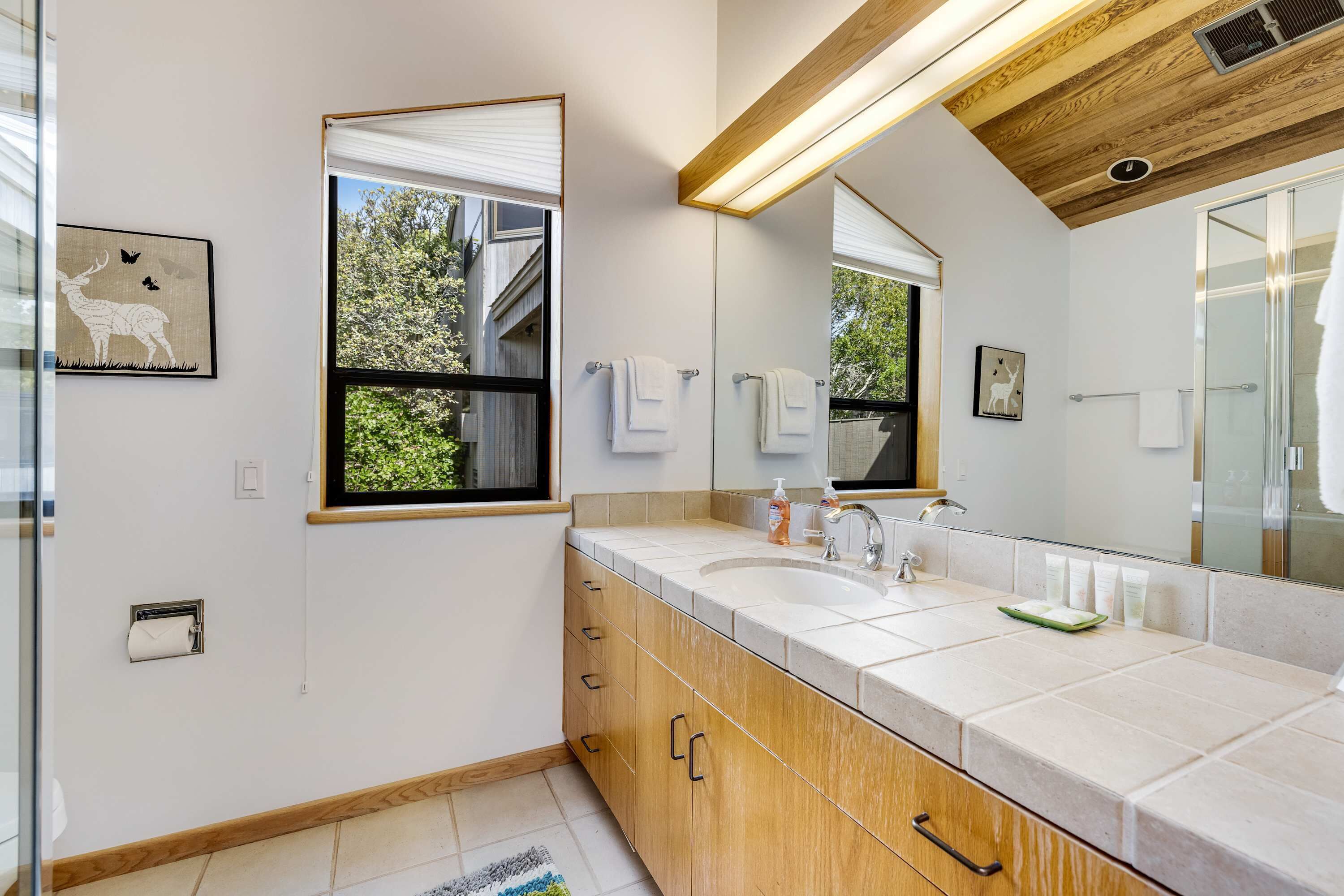 Een moderne badkamer met een grote spiegel, twee wasbakken, houten kastjes en een raam met uitzicht op groen.