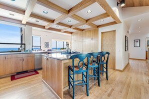A modern kitchen with wooden beams, a large island, bar stools, and a view of the ocean. - Sea Ranch 4BR architectural home with ocean views & private hot tub (Sea Ranch)