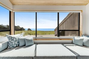A modern room with a large window, a built-in bench with cushions, and a view of the sea. - Sea Ranch 4BR architectural home with ocean views & private hot tub (Sea Ranch)