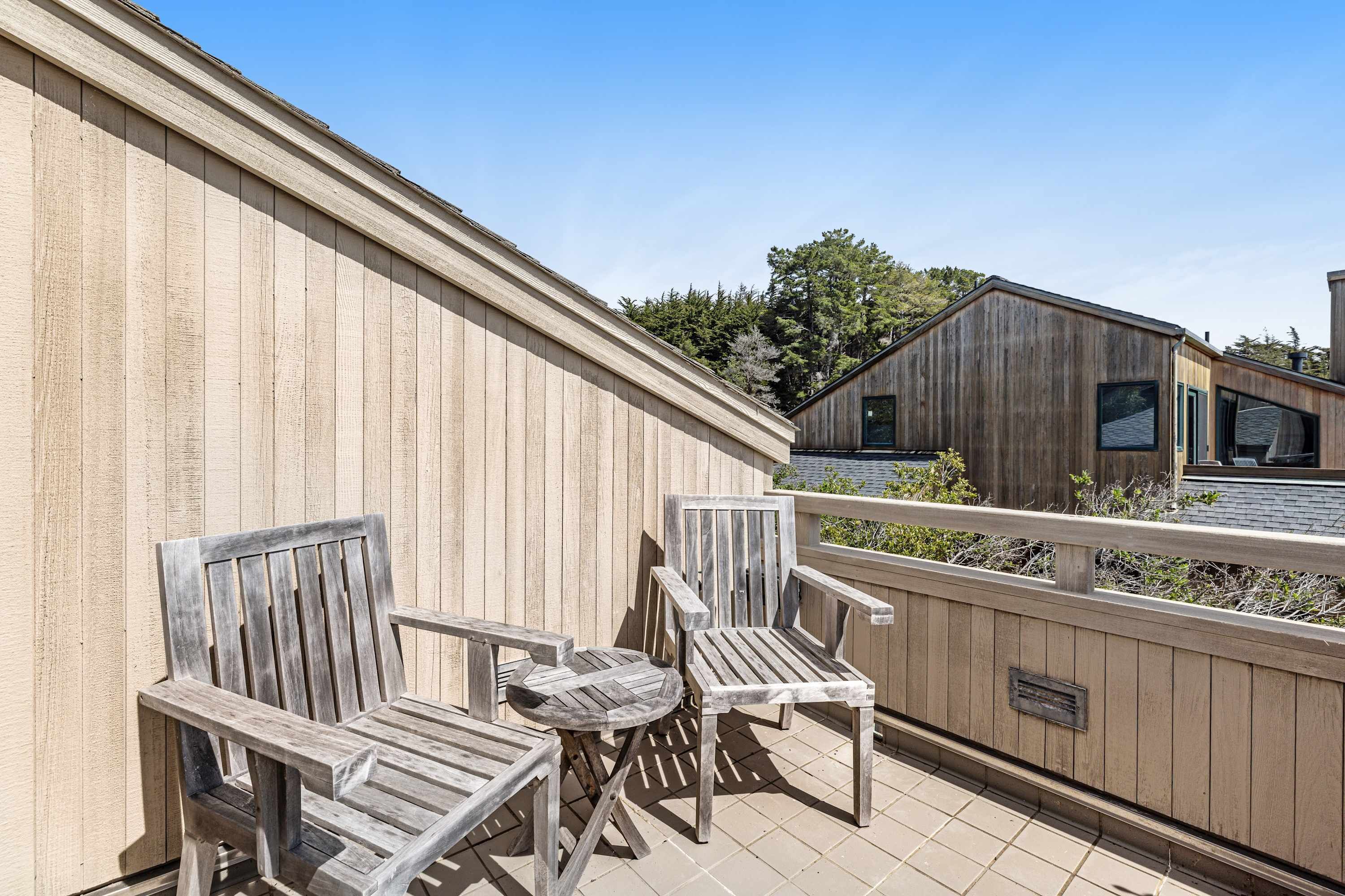 Une terrasse en bois avec deux chaises et une petite table ronde, une clôture en bois et un bâtiment en arrière-plan.