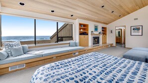 Ein Schlafzimmer mit einem großen Bett, einer eingebauten Sitzbank, einer Holzbalkendecke und Meerblick.